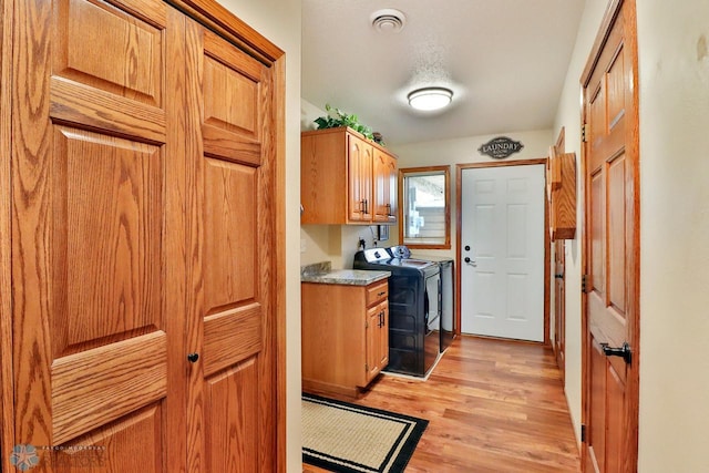 laundry room with washing machine and clothes dryer, visible vents, cabinet space, and light wood finished floors