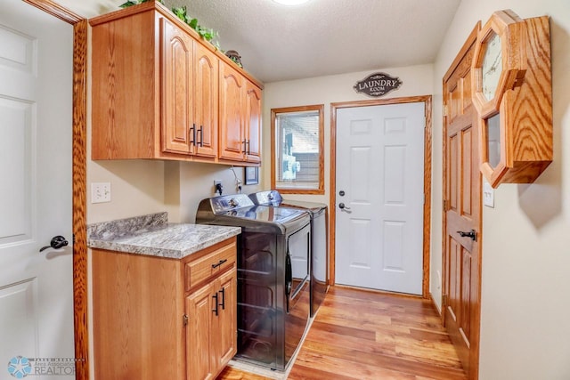 laundry room with light wood-type flooring, cabinet space, separate washer and dryer, and a textured ceiling