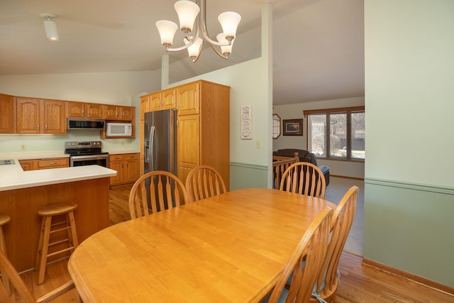 dining area featuring baseboards, lofted ceiling, a notable chandelier, and light wood finished floors