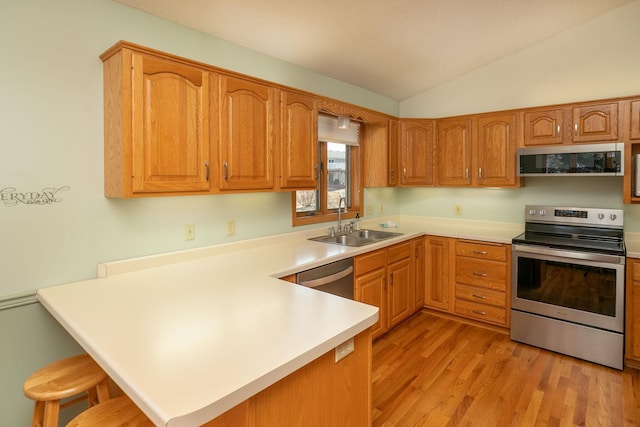 kitchen with a breakfast bar, a sink, appliances with stainless steel finishes, a peninsula, and vaulted ceiling