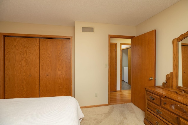 bedroom with baseboards, visible vents, a closet, a textured ceiling, and light carpet