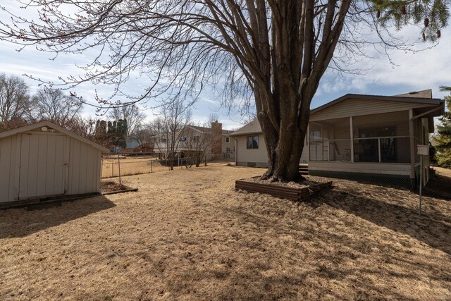 view of yard featuring fence, an outbuilding, a storage shed, and a sunroom