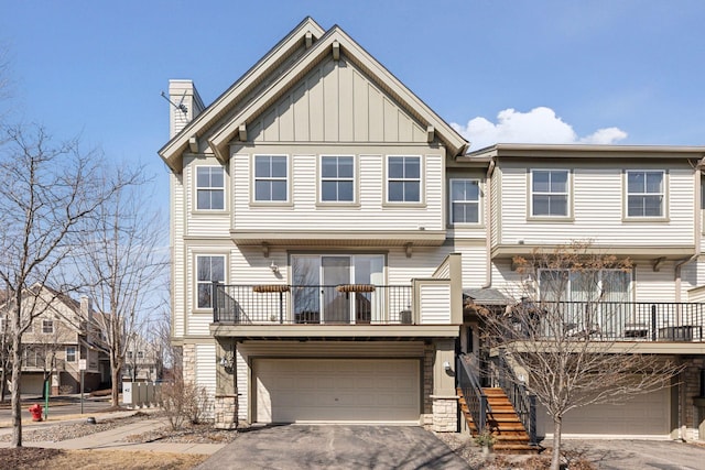 view of property featuring driveway, a chimney, stairs, a garage, and board and batten siding