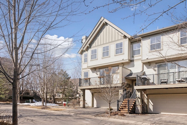 townhome / multi-family property featuring board and batten siding, stairway, a chimney, a garage, and driveway