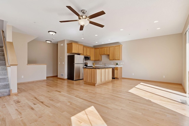 kitchen featuring a center island, light brown cabinetry, open floor plan, light wood-style flooring, and appliances with stainless steel finishes