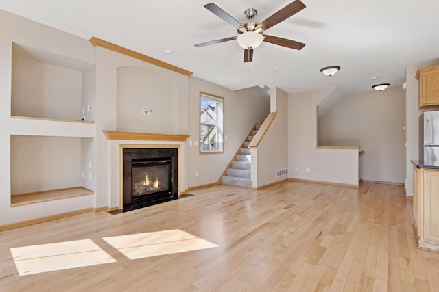 unfurnished living room featuring light wood-type flooring, visible vents, a fireplace with flush hearth, ceiling fan, and stairs