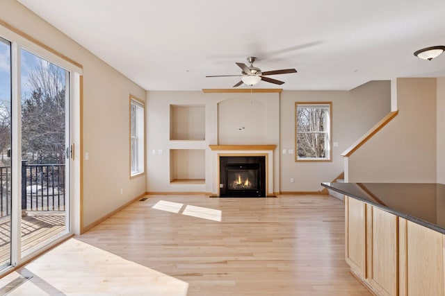 unfurnished living room with light wood-type flooring, a fireplace with flush hearth, baseboards, and stairs