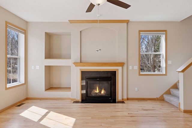 unfurnished living room with stairway, wood finished floors, visible vents, baseboards, and a fireplace with flush hearth