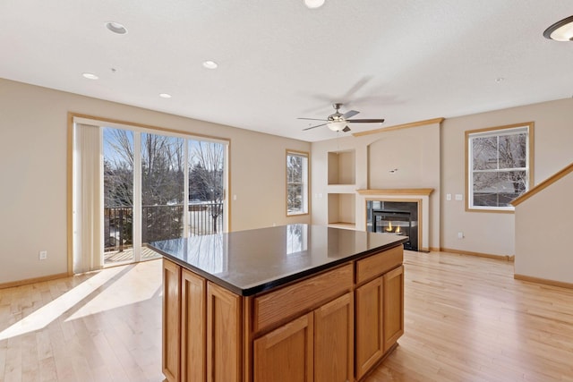 kitchen featuring dark countertops, a kitchen island, baseboards, light wood-type flooring, and a glass covered fireplace