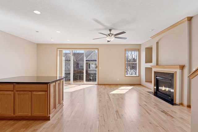 unfurnished living room featuring light wood finished floors, baseboards, a fireplace with flush hearth, a textured ceiling, and a ceiling fan