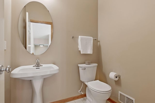 half bath with visible vents, baseboards, toilet, tile patterned floors, and a sink