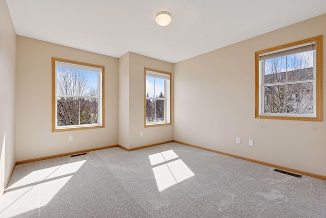 carpeted empty room featuring visible vents, baseboards, and a healthy amount of sunlight