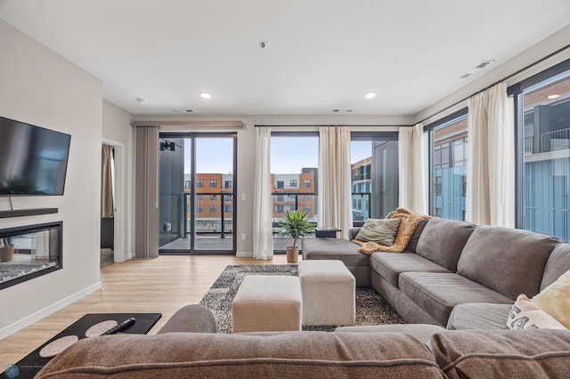 living area with a glass covered fireplace, recessed lighting, light wood-style floors, and baseboards