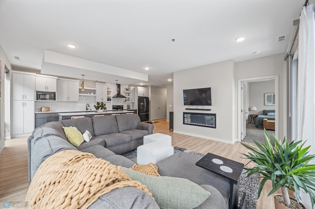 living room with recessed lighting, light wood-type flooring, baseboards, and a glass covered fireplace