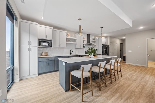 kitchen with a sink, a center island, wall chimney range hood, black appliances, and open shelves