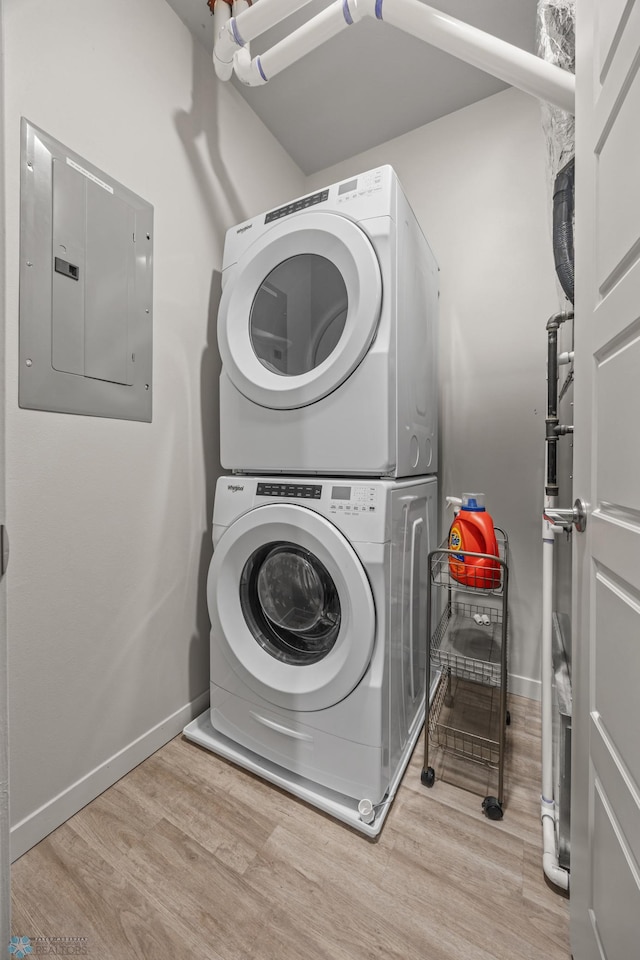 laundry room with wood finished floors, baseboards, laundry area, electric panel, and stacked washer / drying machine