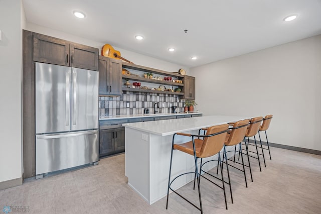 kitchen featuring open shelves, a kitchen breakfast bar, freestanding refrigerator, light countertops, and decorative backsplash