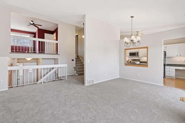 unfurnished living room featuring visible vents, carpet floors, baseboards, stairs, and ceiling fan with notable chandelier