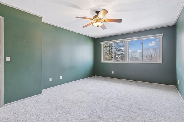 carpeted spare room featuring crown molding, visible vents, baseboards, and ceiling fan