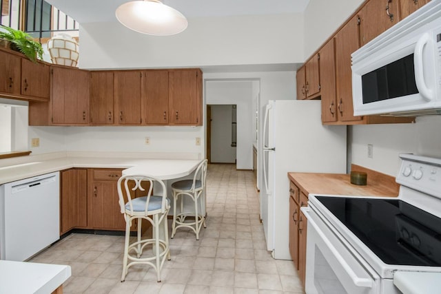 kitchen with brown cabinetry, white appliances, a breakfast bar area, and light countertops