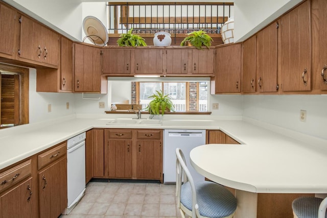 kitchen with light countertops, brown cabinetry, white dishwasher, and a sink