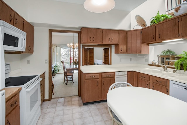 kitchen with white appliances, brown cabinetry, a sink, light countertops, and a notable chandelier