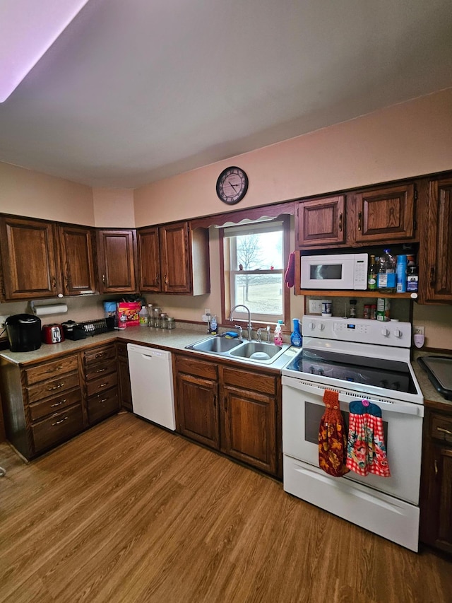 kitchen featuring dark brown cabinets, light wood-style flooring, white appliances, and a sink