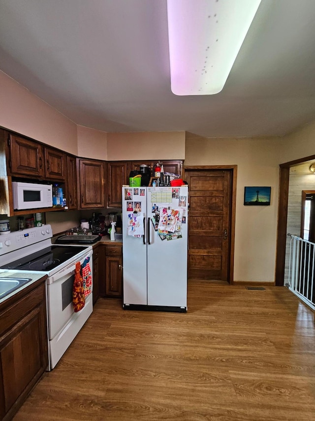 kitchen featuring white appliances, dark brown cabinetry, and light wood finished floors