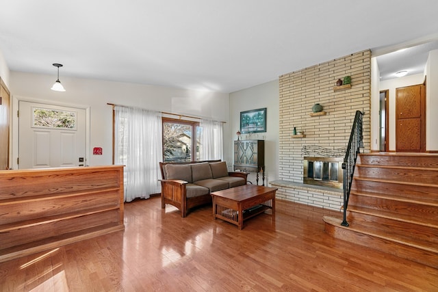 living room with a brick fireplace, stairs, and wood finished floors