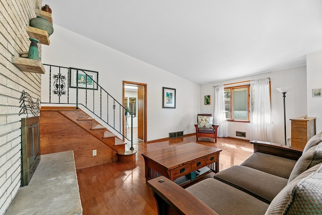 living room with wood finished floors, visible vents, lofted ceiling, stairs, and a brick fireplace