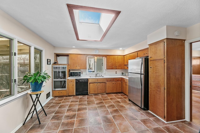 kitchen with light countertops, brown cabinets, appliances with stainless steel finishes, a skylight, and a sink