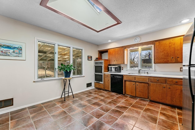 kitchen with brown cabinetry, visible vents, a sink, stainless steel appliances, and light countertops