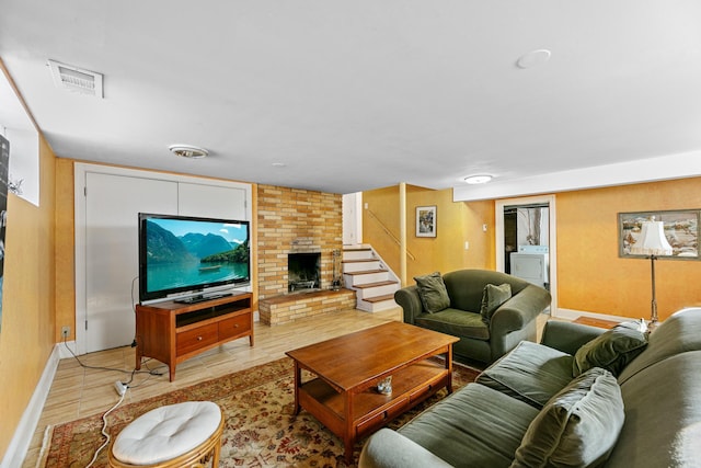 living area featuring visible vents, washer / dryer, a brick fireplace, and stairs