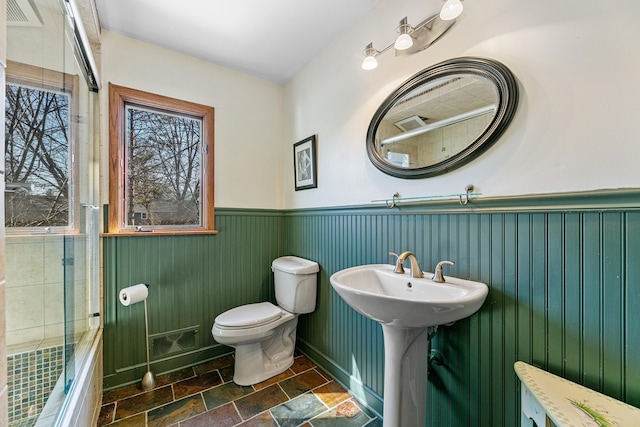 bathroom featuring visible vents, wainscoting, stone finish flooring, shower / bath combination, and toilet