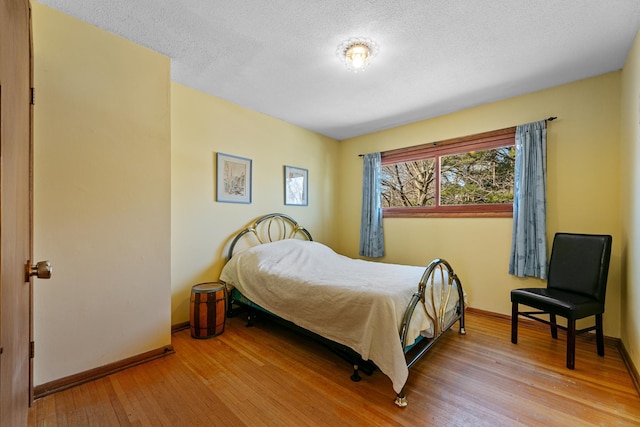 bedroom with a textured ceiling, light wood-type flooring, and baseboards