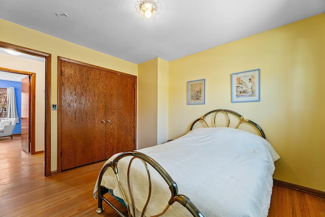 bedroom with a closet, light wood-type flooring, and baseboards