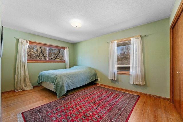 bedroom featuring a closet, a textured ceiling, baseboards, and wood finished floors