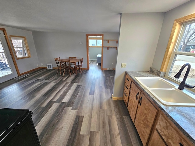 kitchen with brown cabinetry, baseboards, visible vents, dark wood-style flooring, and a sink