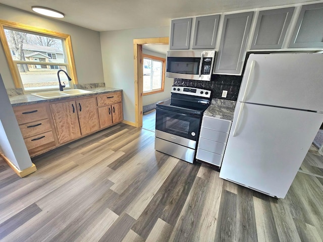 kitchen featuring a sink, wood finished floors, stainless steel appliances, decorative backsplash, and baseboards