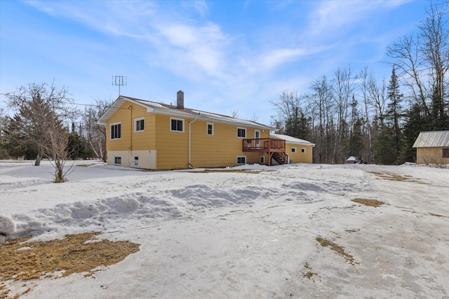 snow covered house featuring a deck, stairs, and a chimney