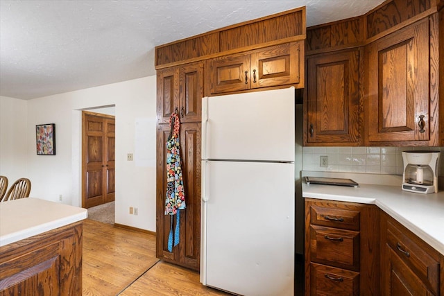 kitchen featuring light wood-style flooring, freestanding refrigerator, light countertops, a textured ceiling, and backsplash