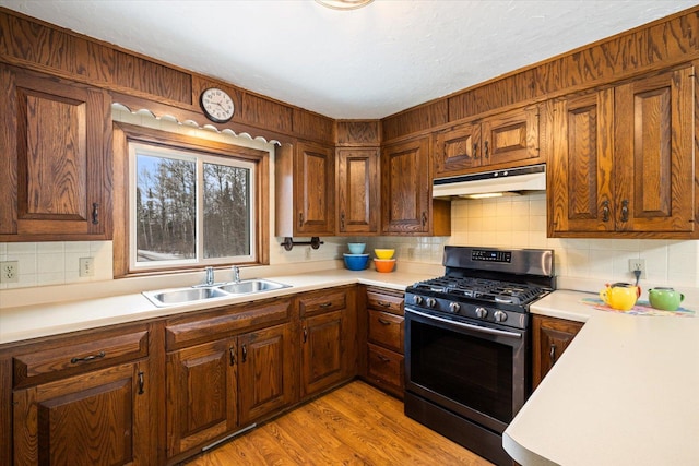 kitchen with light countertops, stainless steel gas range, under cabinet range hood, and a sink