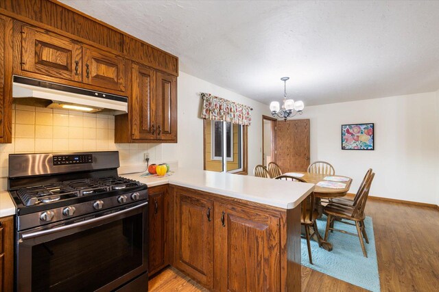 kitchen with a peninsula, light countertops, under cabinet range hood, stainless steel gas range oven, and light wood-type flooring