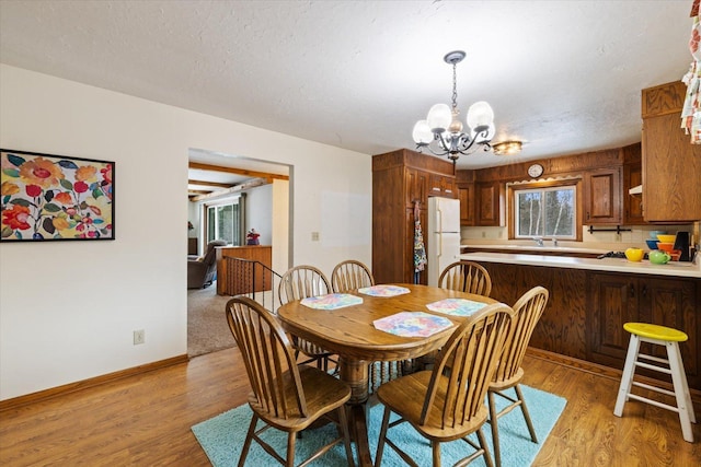 dining area with a chandelier, baseboards, a textured ceiling, and light wood-style flooring