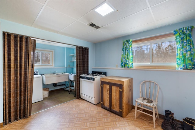 kitchen featuring visible vents, a sink, a drop ceiling, gas range gas stove, and washer / clothes dryer