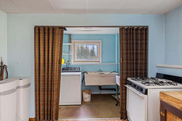 kitchen featuring white gas stove, a sink, washer / clothes dryer, concrete floors, and light countertops