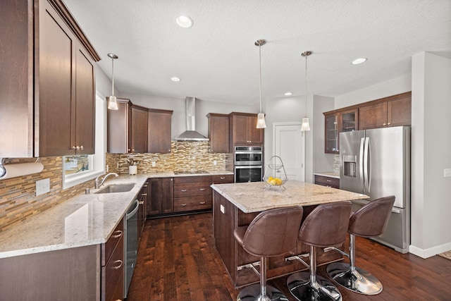 kitchen featuring a kitchen island, dark wood finished floors, a sink, stainless steel appliances, and wall chimney exhaust hood