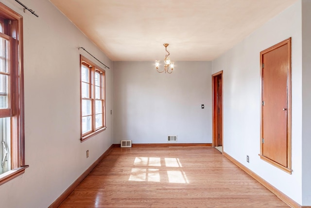 empty room with an inviting chandelier, baseboards, visible vents, and light wood finished floors