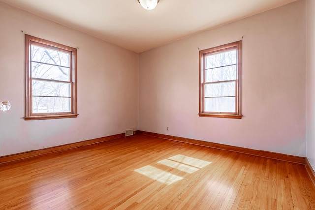 spare room featuring light wood finished floors, visible vents, baseboards, and a wealth of natural light