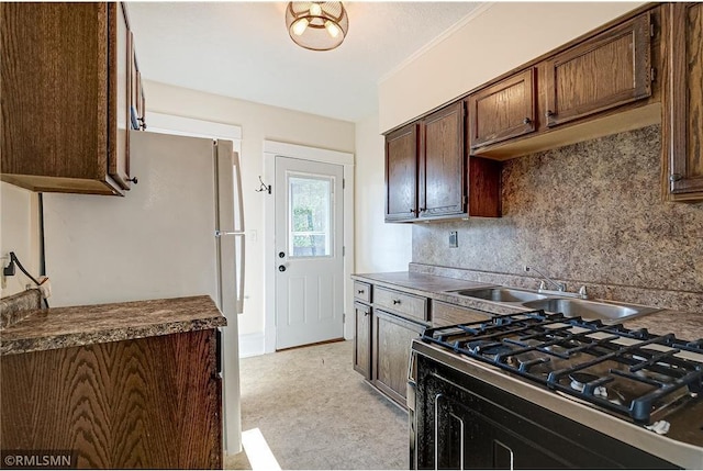 kitchen with dark countertops, backsplash, dark brown cabinets, stovetop, and a sink